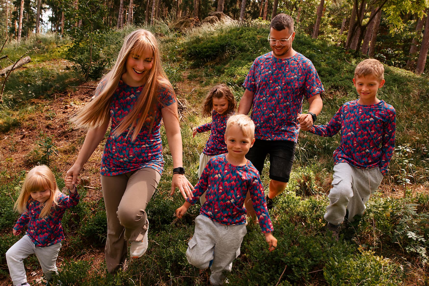 Familie trägt Merino T-Shirts mit buntem Bergmotiv von Bellibell bei einem gemeinsamen Spaziergang im Wald.