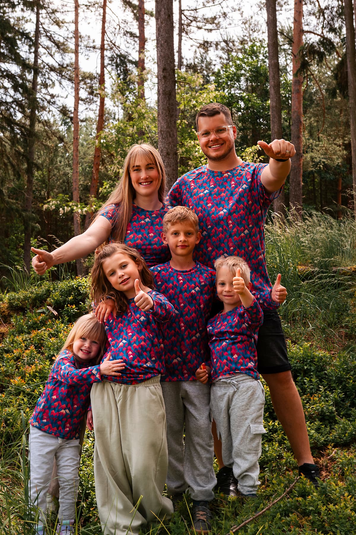 Familie trägt Merino Shirts mit buntem Bergmotiv von Bellibell bei einem Ausflug im Wald.