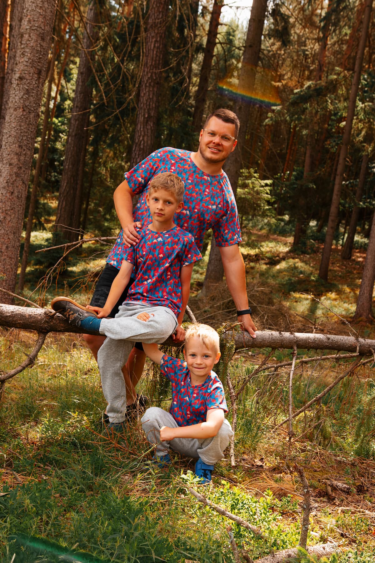 Familie trägt farbenfrohe Merino T-Shirts mit Bergmotiv von Bellibell bei einem Ausflug im Wald.