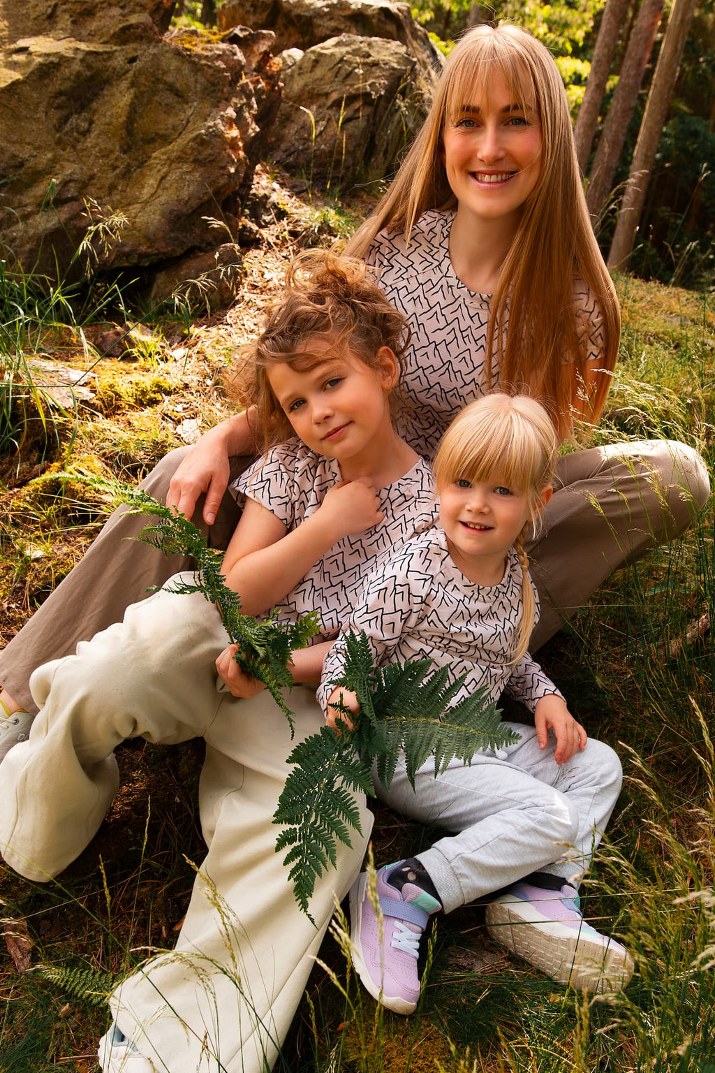 Mutter und Kinder tragen Merino T-Shirts mit Bergmotiv von Bellibell bei einem Familienausflug im Wald.