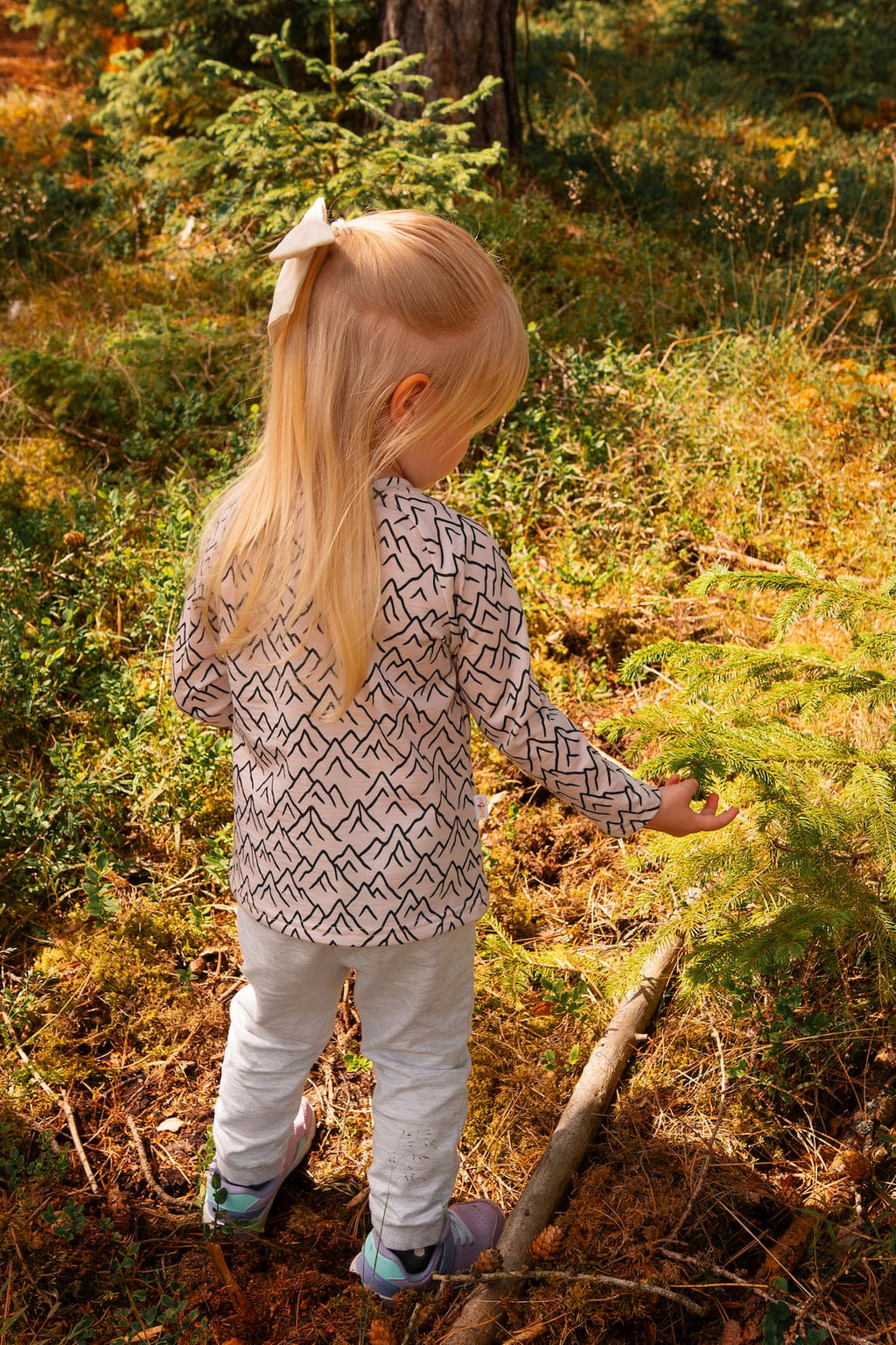 Rückansicht eines Merino Kinder-Langarmshirts mit grauem Bergmotiv von Bellibell im Wald.