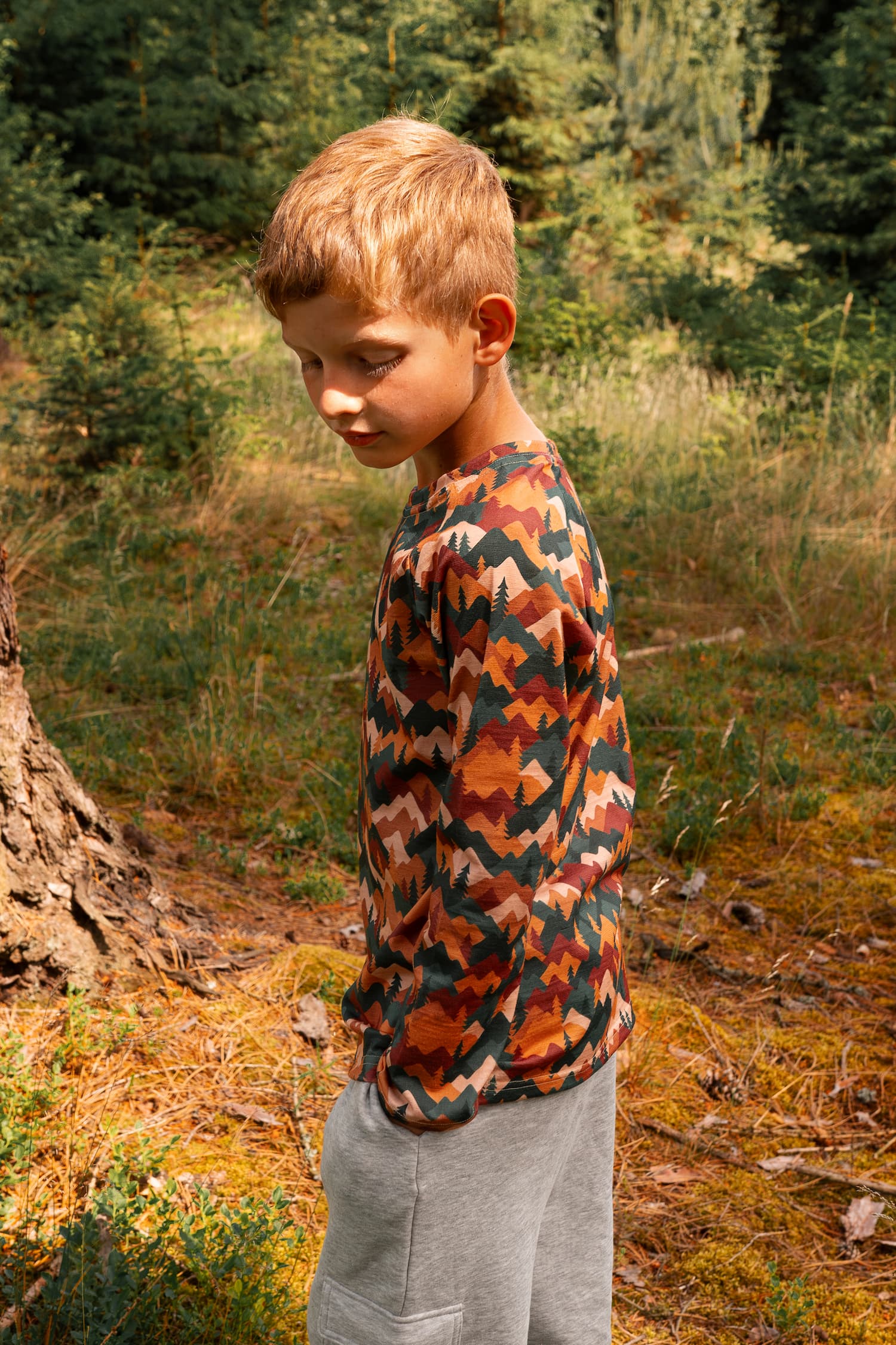 Junge trägt ein Merino Kinder-Langarmshirt mit Herbst-Bergmotiv von Bellibell im Wald.