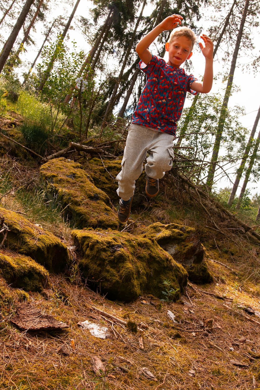 Junge springt im Wald und trägt ein buntes Merino Kinder T-Shirt mit Bergmotiv von Bellibell.