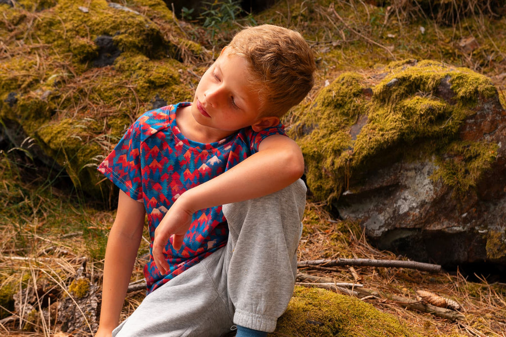 Junge trägt ein buntes Merino Kinder T-Shirt mit Bergmotiv von Bellibell beim Spielen im Wald.