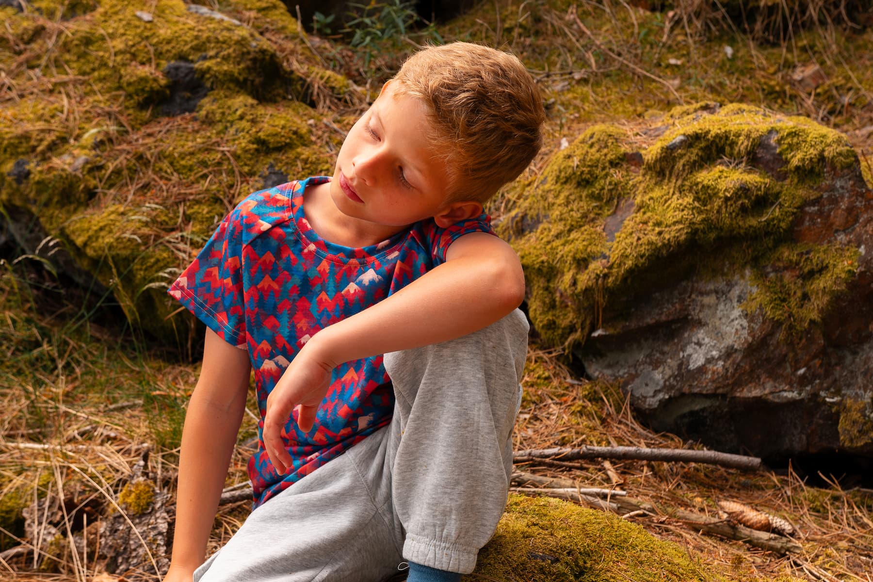 Junge trägt ein buntes Merino Kinder T-Shirt mit Bergmotiv von Bellibell beim Spielen im Wald.