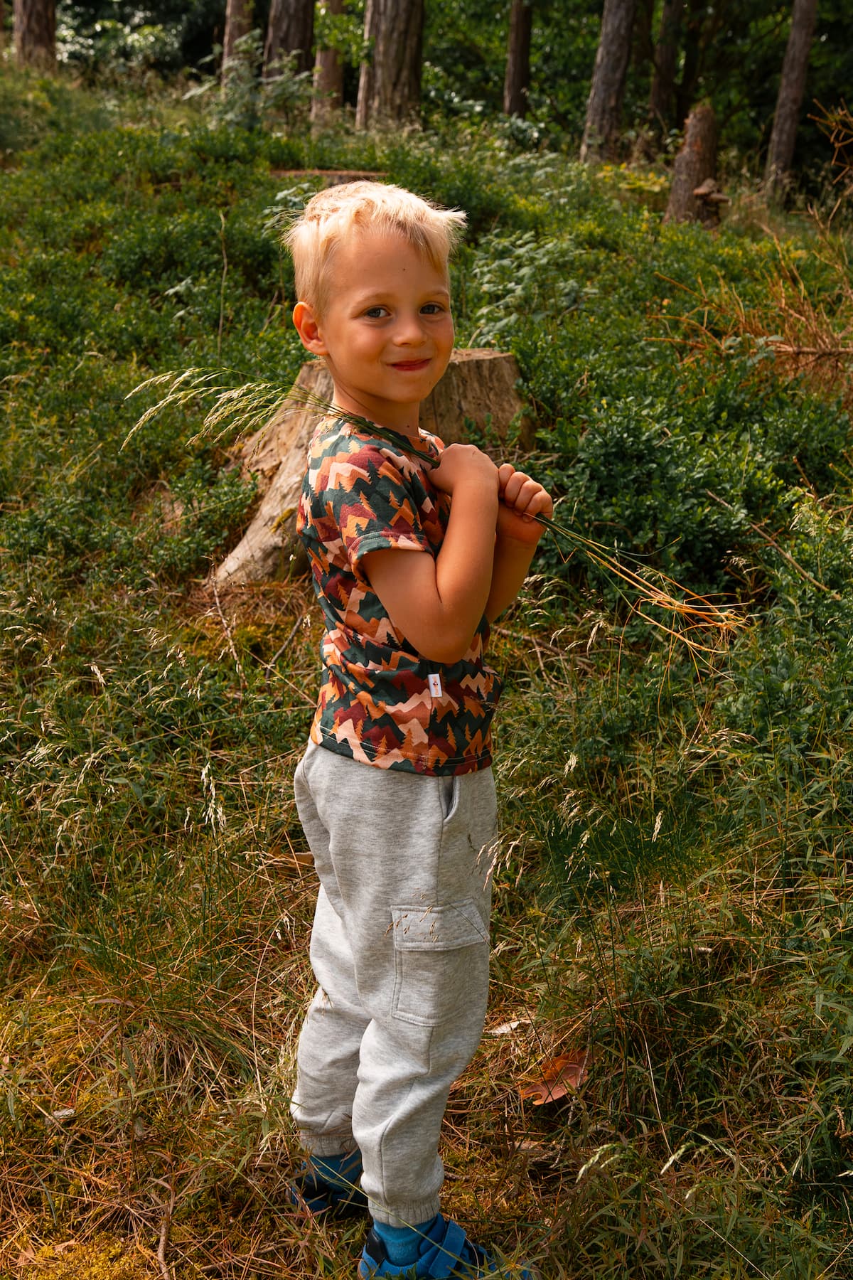 Junge trägt ein Merino Kinder T-Shirt mit Herbst-Bergmotiv von Bellibell und steht im Wald.