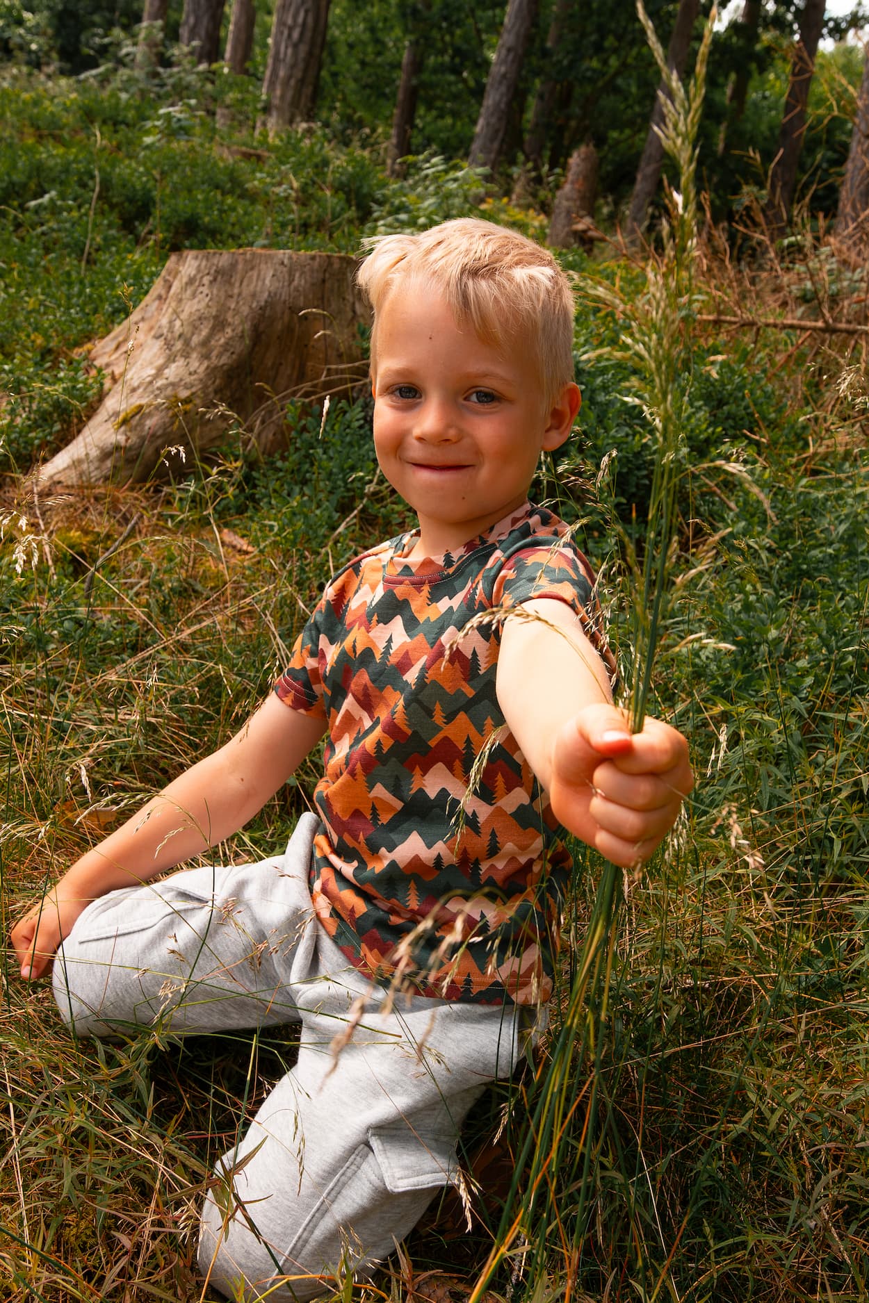 Junge trägt ein Merino Kinder T-Shirt mit Herbst-Bergmotiv von Bellibell und sitzt im Wald.