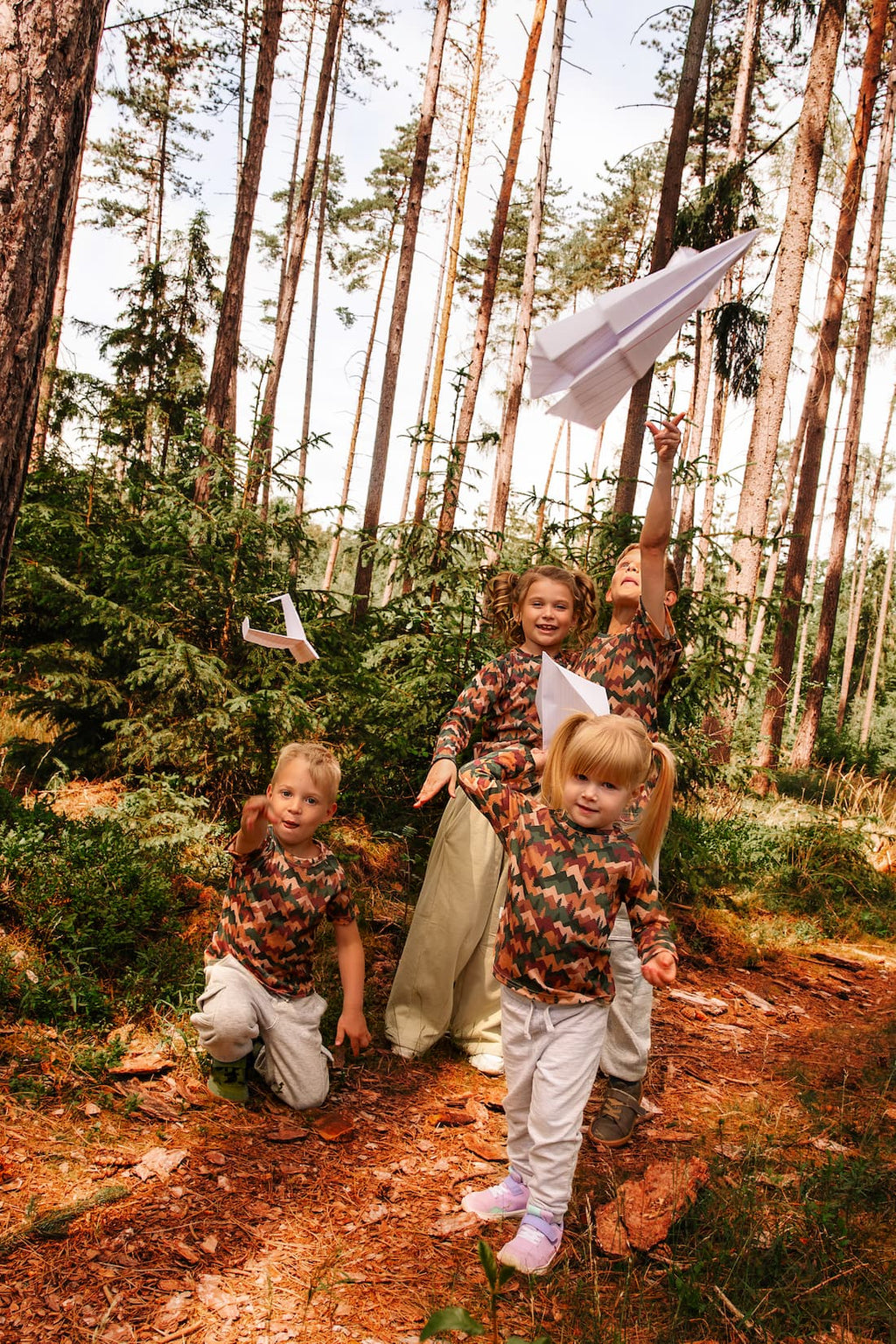 Kinder tragen Merino T-Shirts mit Herbst-Bergmotiv von Bellibell und spielen mit Papierfliegern im Wald.