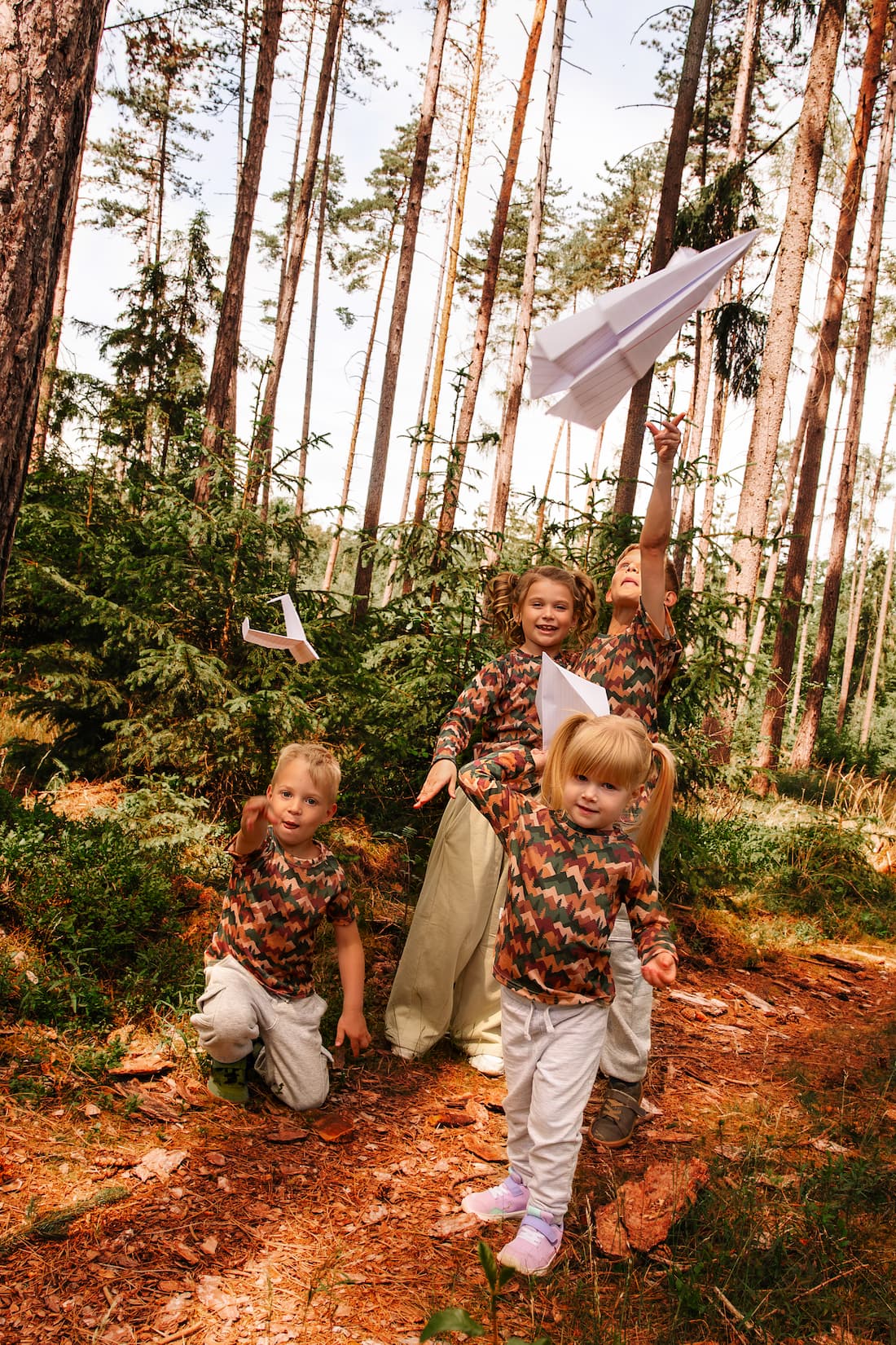 Kinder tragen Merino T-Shirts mit Herbst-Bergmotiv von Bellibell und spielen mit Papierfliegern im Wald.