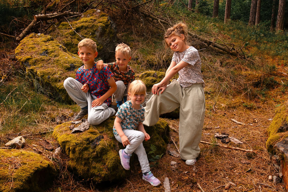 Kinder tragen Merino Kinder-T-Shirts von Bellibell und verbringen gemeinsam Zeit im Wald.